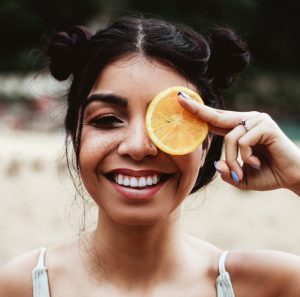 woman holding lemon slice in front of eye and smiling
