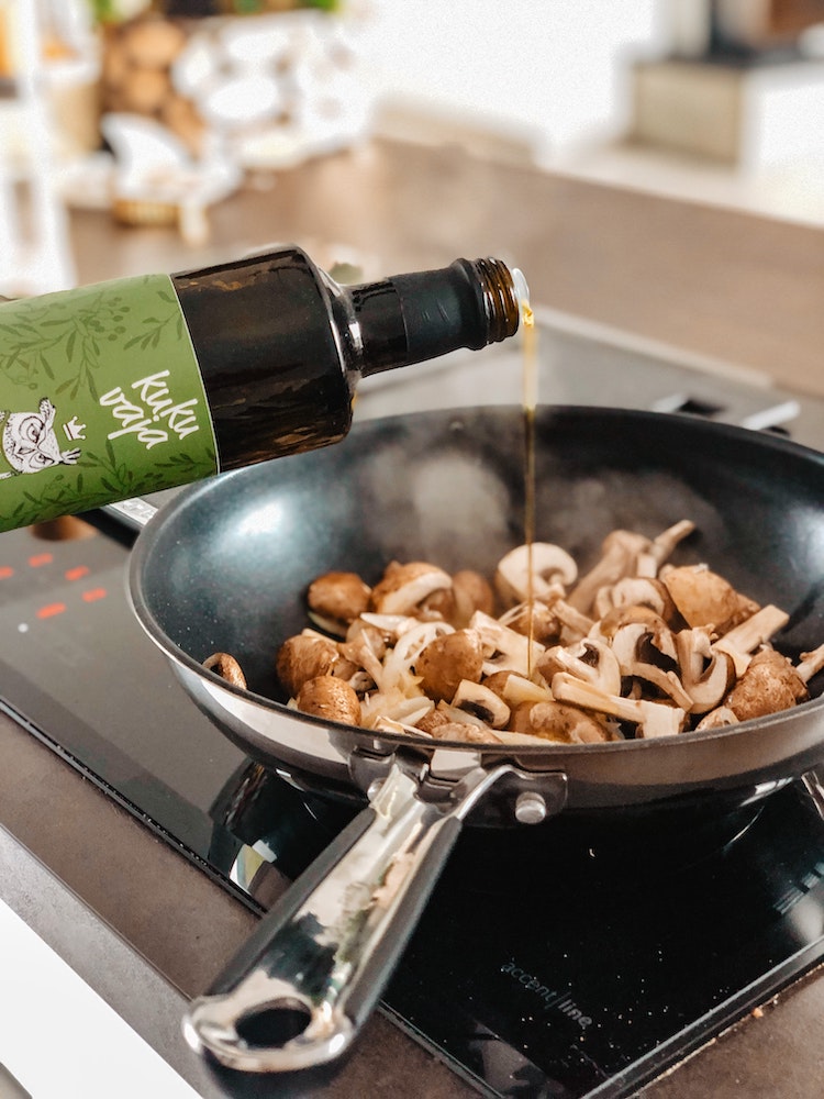 Mushrooms sizzling in a pan with a bottle of oil being drizzled over