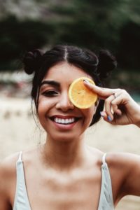 woman smiling holding lemon slice in front of eye