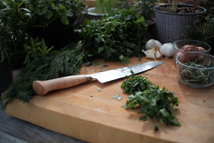 chefs knife with wooden handle on wooden cutting board with chopped herbs