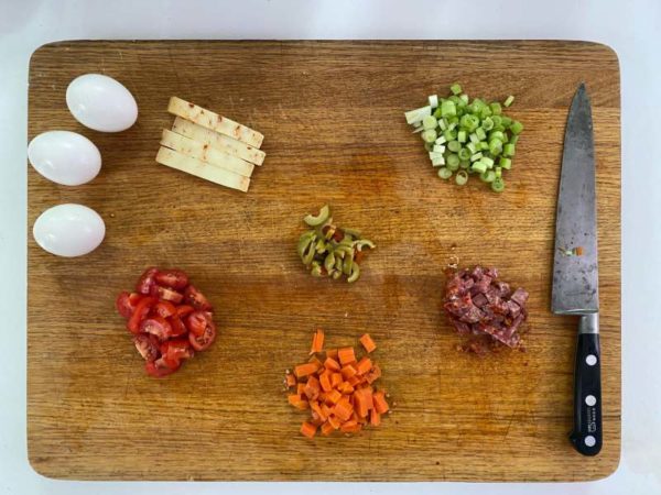 wooden cutting board with sliced veggies and whole eggs