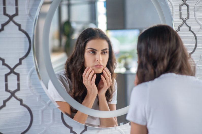 woman looking in the mirror at adult acne