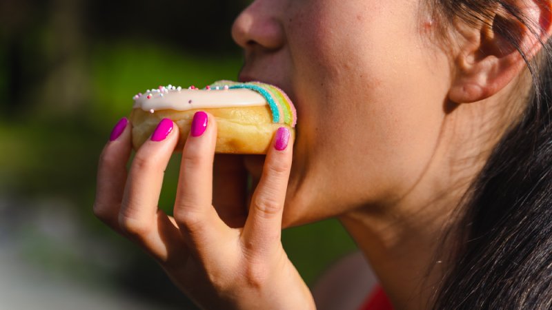 woman with pink fingernails eating a donut