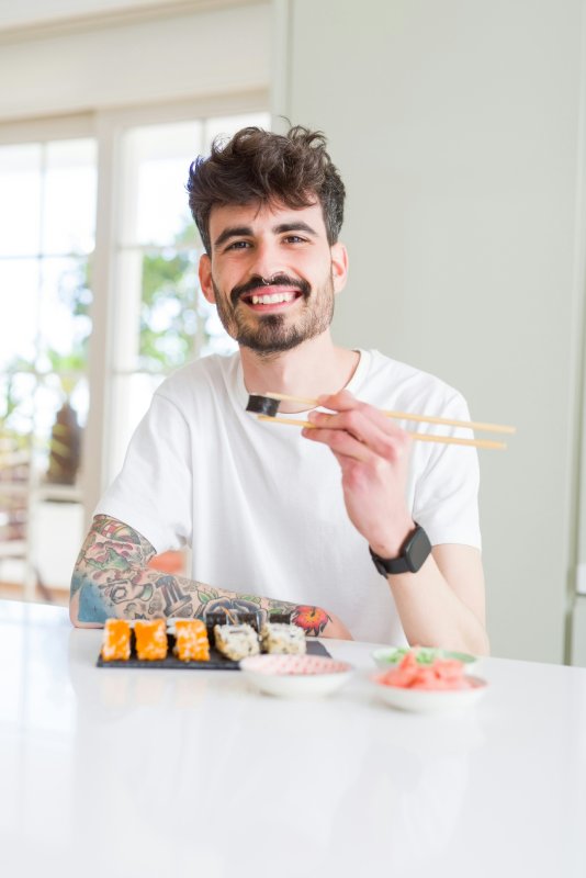 man smiling and holding chopsticks and sushi roll